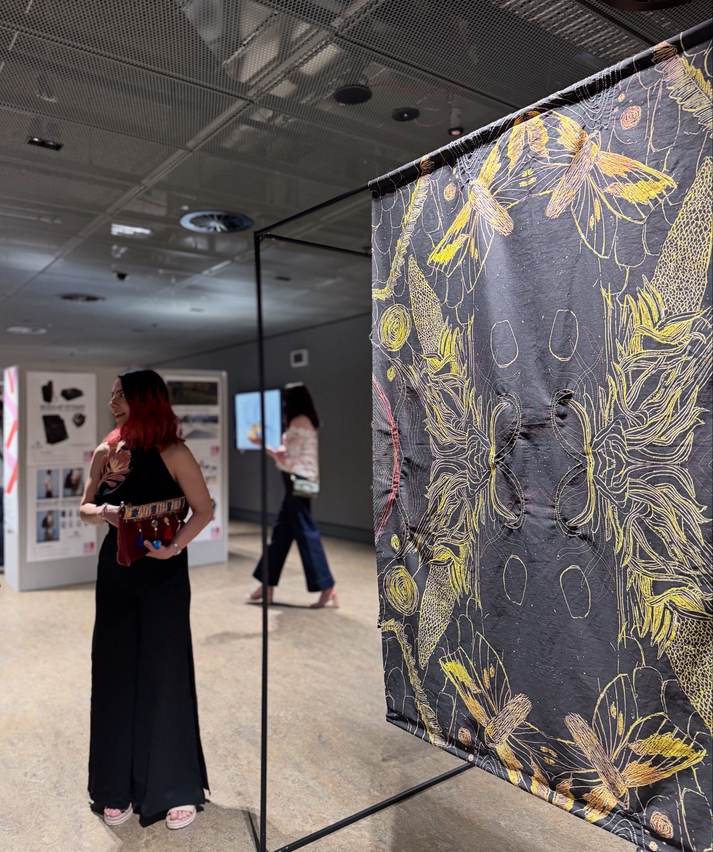 Maral Mahlouji at the Ember and Bloom exhibition beside a hand-embroidered textile panel